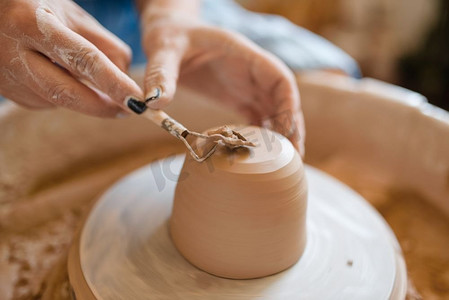 陶瓷摄影照片_女陶工除去壶、陶轮上多余的一层。女人塑造一个碗。手工陶艺，用粘土制作的餐具