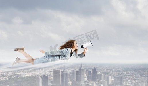 女超人摄影照片_会飞的女超人。年轻漂亮的女商人飞在蓝天上，拿着扩音器欢笑