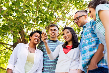 友谊，技术和国际概念—一群朋友与智能手机在夏季公园。快乐的朋友与智能手机在夏季公园