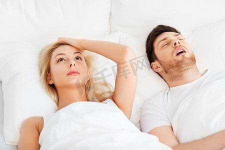 睡眠问题和人的概念—不愉快的女人躺在床上与打鼾的男人不愉快的女人在床上与打鼾睡觉的男人