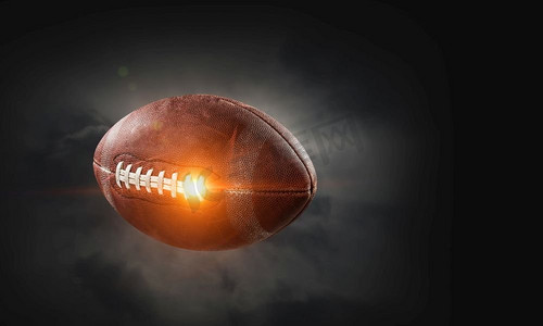 游戏爆炸背景摄影照片_黑暗背景下闪电中的橄榄球。混合媒体。美式橄榄球比赛