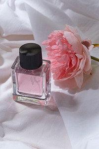 美丽，香水和对象概念—瓶香水和花在白色床单与折叠。一瓶香水和花在白色床单