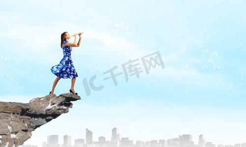 吹长笛的女人。一位身穿蓝色连衣裙的年轻女子站在岩石上吹奏长笛