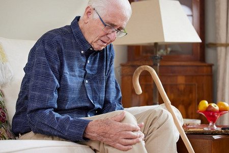 老年男子坐在沙发上在家遭受关节炎的膝盖疼痛