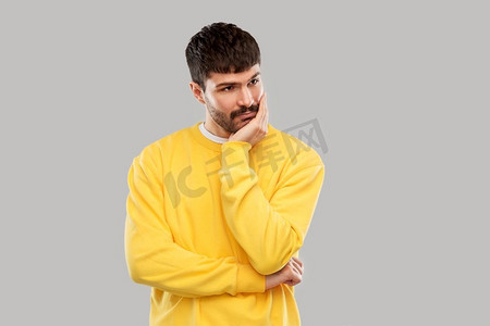 人物灰色摄影照片_人物概念-穿着黄色运动衫的悲伤年轻人在灰色背景下思考。穿着黄色运动衫的悲伤的年轻人在想