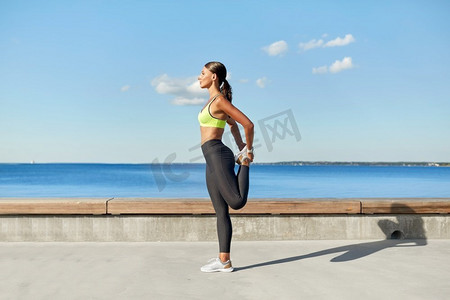 健身，运动和健康的生活方式概念—年轻妇女伸展腿在海滨长廊。快乐的年轻女子做运动和伸展腿