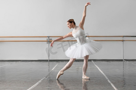 美丽的女芭蕾舞演员在芭蕾舞课，barre和白色墙背景。美丽的女芭蕾舞演员在类