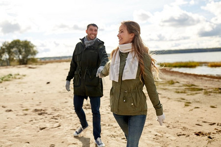 爱情、关系和人情观--一对微笑的情侣手牵手漫步秋日海滩。一对情侣沿着秋天的海滩散步