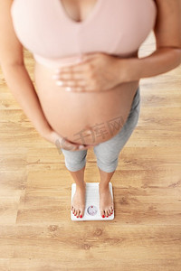 怀孕，体重控制和饮食概念—孕妇站在家里的秤上。孕妇站在家里秤上