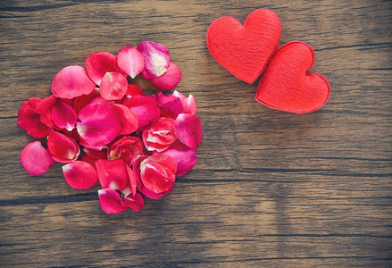 情人节爱心概念/堆玫瑰花瓣与红色的心脏装饰在木桌乡村背景 