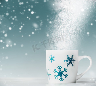 蓝色雪花摄影照片_白色桌子上有蓝色雪花的白色马克杯，蓝色背景上有雪和波克，前景。寒假快乐卡片排版