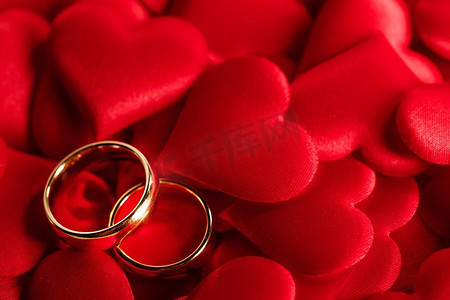 两个金结婚戒指在红缎心背景。金色结婚戒指在红色
