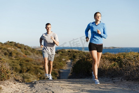 健身情侣摄影照片_运动跑步者在海滩上慢跑，和她的伴侣一起锻炼。健康的女健身模特和她的伴侣沿着海洋慢跑