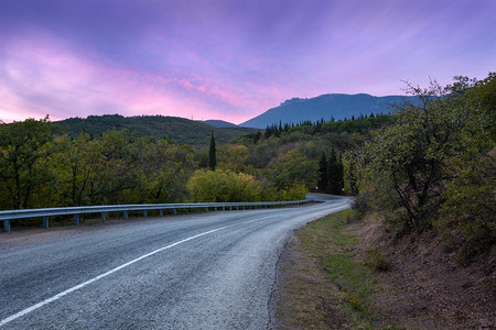 山蜿蜒的道路通过森林与五颜六色的天空在日落在夏天