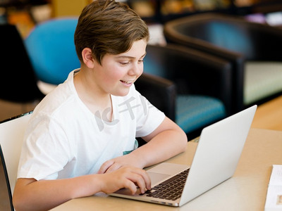 十几岁的男孩坐在图书馆里，手里拿着平板电脑。十几岁的男孩在图书馆里拿着平板电脑