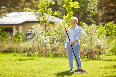 草坪和人摄影照片_园艺和人的概念快乐的老年妇女与草坪犁在夏园工作。拿着草坪犁的老妇人在花园里干活