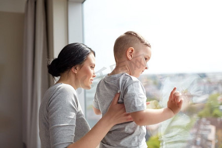 人和家庭的概念-快乐的母亲和小儿子在家里透过窗户看着。母子俩在家中透过窗户看着