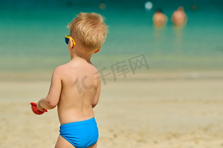 一个蹒跚学步的男孩在海滩上玩铲子和沙子。两岁的学步男孩在海滩上玩铲子和沙子