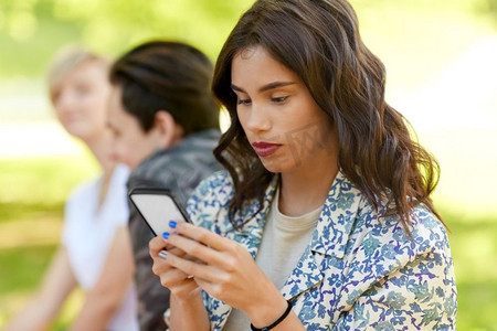 休闲，技术和人的概念—妇女使用智能手机与朋友在夏季公园。妇女使用智能手机与朋友在夏季公园
