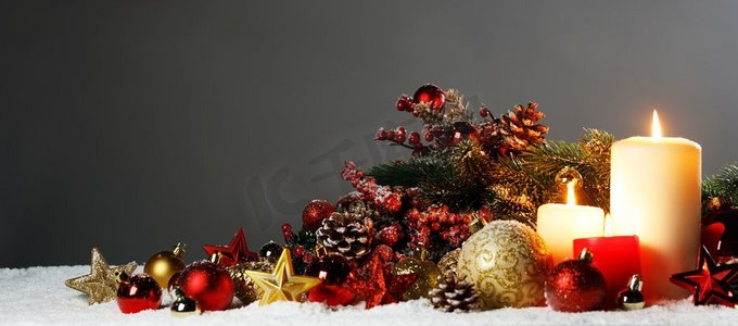 燃烧圣诞蜡烛与红色和金色的装饰星，小玩意儿，松果和绿色的树枝在雪。圣诞蜡烛装饰