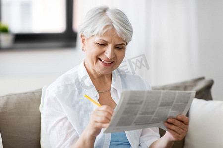 年龄和人的概念—老年妇女在家中标记报纸广告。老年妇女在家中标记报纸广告