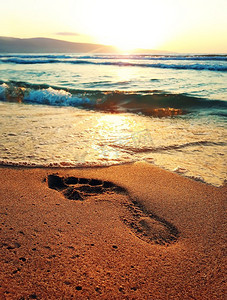 人类的脚摄影照片_人类的足迹在海滩金色的沙滩前的日出在海上。