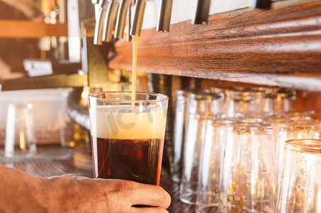 调酒师用手从酒吧的水龙头往玻璃杯里倒生啤酒。酒吧服务员正在用水龙头供应啤酒。