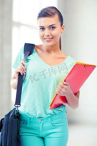 快乐的女学生背着书包和彩色文件夹。背着书包和彩色文件夹的女学生