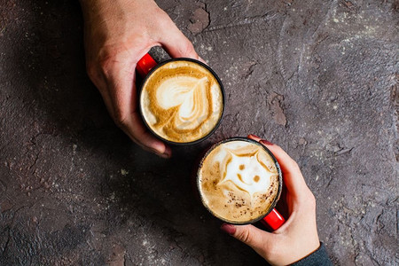 两只手拿着热咖啡在黑暗的背景下，俯视。为相爱的情侣提供早餐咖啡