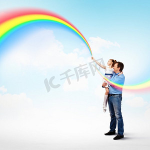 彩虹儿童摄影照片_父亲抱着女儿和彩虹。幸福的父亲牵着女儿的手形象和彩虹