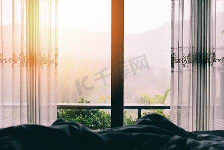 窗户视图自然绿色山在床上在卧室早上和阳光/窗户玻璃与窗帘 