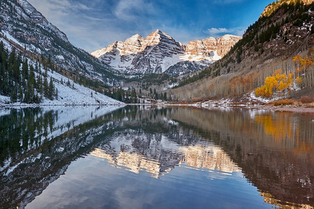 钟声摄影照片_栗色的钟声和栗色的湖与岩石和山在雪周围的反射在秋天在科罗拉多落基山脉，美国。 