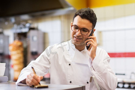 人、快餐和烹饪概念-烤肉店的厨师在智能手机上写订单和打电话。烤肉店的厨师用智能手机呼叫