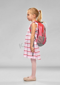 童年、教育和人的概念--快乐的女学生，背着灰色背景的书包。快乐的女学生背着书包