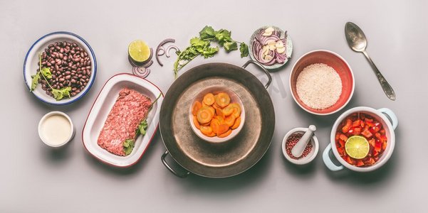 配料的碗与豆子、碎肉、米饭和蔬菜在灰色背景上平放一锅饭，俯视，平放