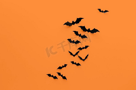 万圣节装饰概念-橙色背景上的许多黑色纸蝙蝠。橙色背景的黑色万圣节蝙蝠