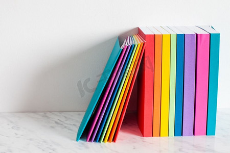 彩色书籍以彩虹的颜色勾勒出轮廓。把书堆在白墙附近的书架上。五颜六色的藏书