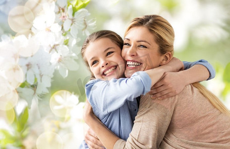 樱花png摄影照片_人和家庭观念--幸福微笑的母亲抱着女儿越过樱花的背景。幸福的母亲在樱花上拥抱女儿