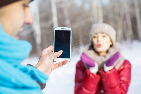 在冬季公园散步。冬日公园里的一位年轻男子在为他的女朋友拍照