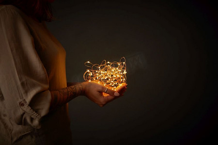在一个女人的手中一个圣诞花环的灯在黑暗的背景。圣诞灯花环在女性手中