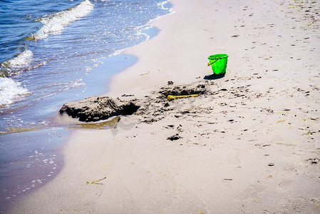 一个孩子在沙滩上留下的绿色玩具桶。有人在海边的沙滩上玩耍。沙滩上的绿色玩具桶