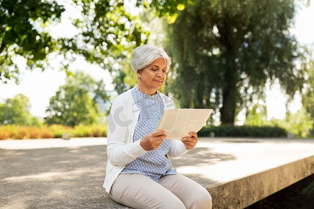 老年、新闻和大众媒体概念—在夏季公园读报的老年妇女。高级妇女阅读报纸在夏季公园