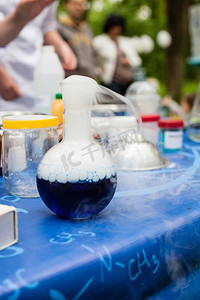 桌上摆着各种各样的化学器皿。前面是一个烧瓶，里面有化学反应。科学化学实验