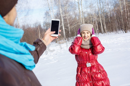 在冬季公园散步。冬日公园里的一位年轻男子在为他的女朋友拍照