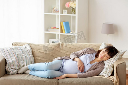 睡觉做梦摄影照片_怀孕、休息、人与期待的概念--快乐的孕妇睡在家里的沙发上。快乐的孕妇睡在家里的沙发上
