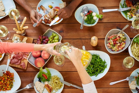 吃和休闲概念-吃晚餐和饮用水的一群人在桌与食物。人们在餐桌上吃东西和喝东西