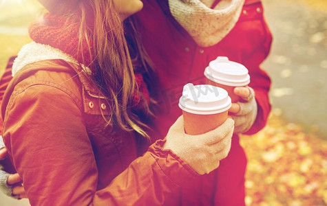 爱情，饮料和人的概念-秋季公园里幸福的年轻情侣拿着咖啡杯的特写。秋天，幸福的情侣喝着咖啡的特写