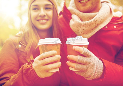爱情，饮料和人的概念-秋季公园里幸福的年轻情侣拿着咖啡杯的特写。秋天，幸福的情侣喝着咖啡的特写