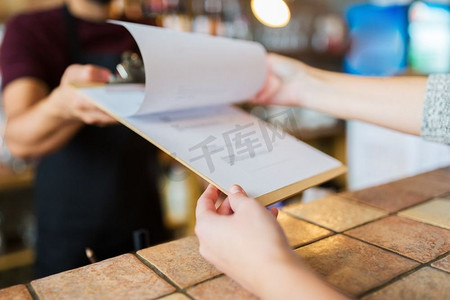 小企业、人和服务理念-酒吧或咖啡店的调酒师向顾客展示菜单。酒吧里的调酒师向顾客展示菜单