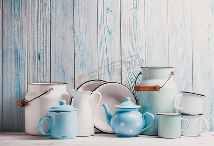 厨房桌子上的搪瓷器皿，上面是蓝色的木质墙壁。珐琅器皿静物